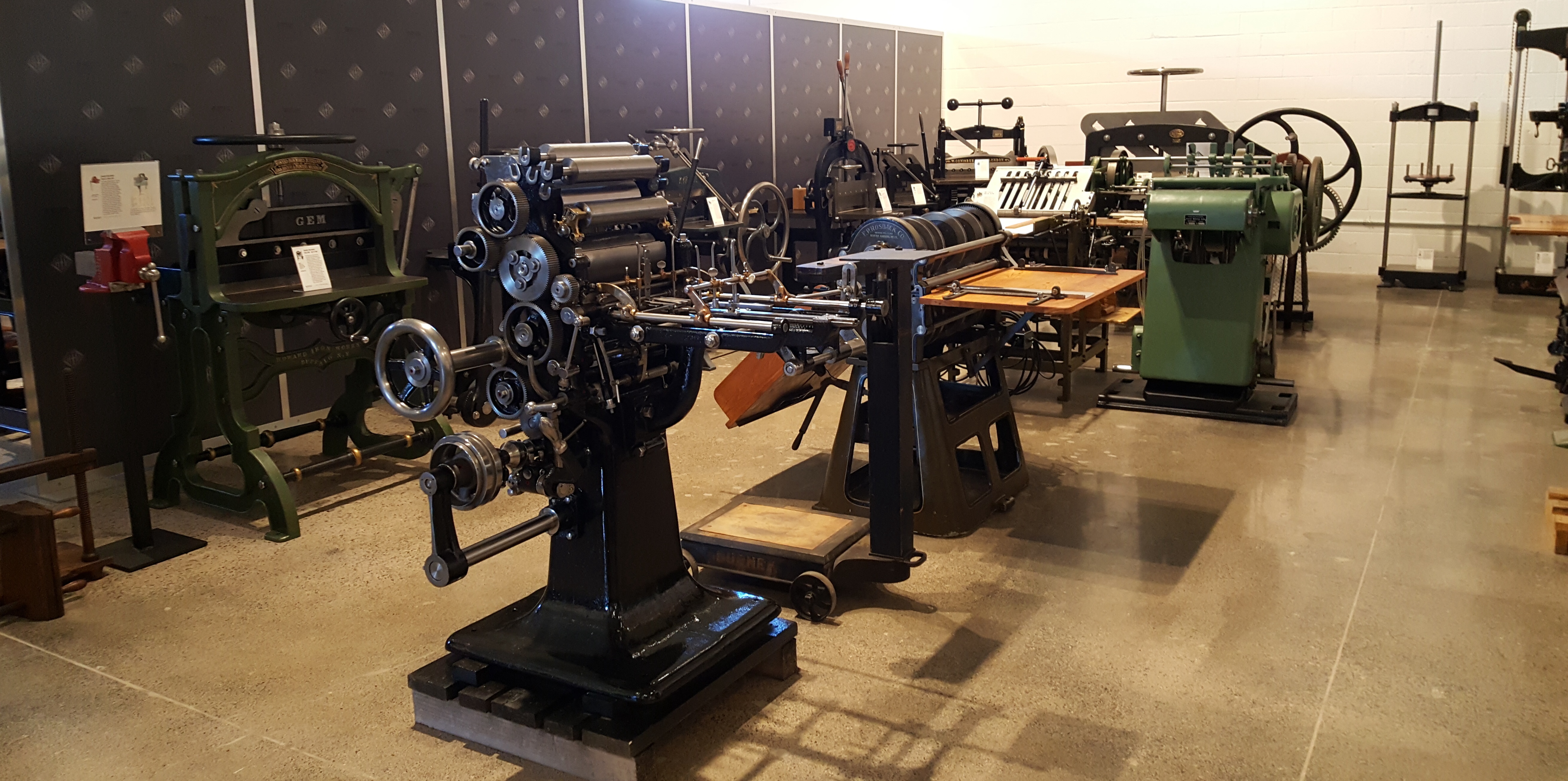 Another bay, containing guillotines, bookbinding presses, a rotary pin perforator, and in the foreground, a very compact and photogenic sheet-fed rotary press.